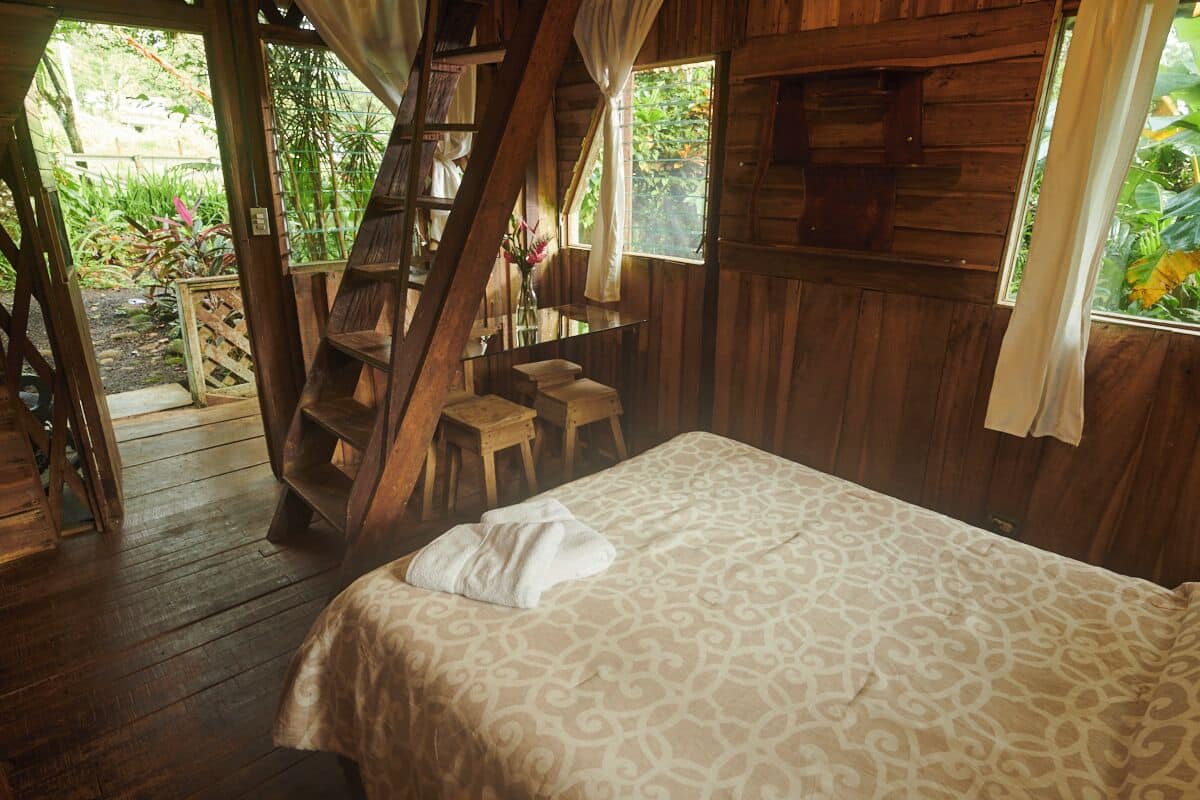 A wooden cabin with a bed, a staircase, and a small seating area with chairs.