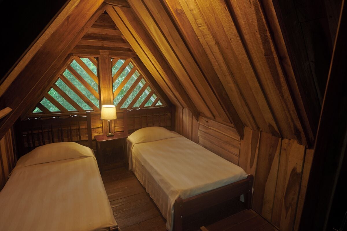 Quarto de sótão aconchegante com duas camas, uma mesinha de cabeceira e um abajur.