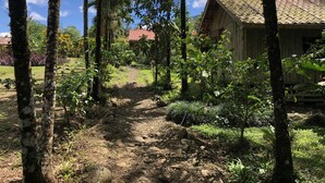 Un bâtiment rustique en bois, doté d’un toit en tuiles, entouré d’une végétation luxuriante et bordé d’un chemin de terre.