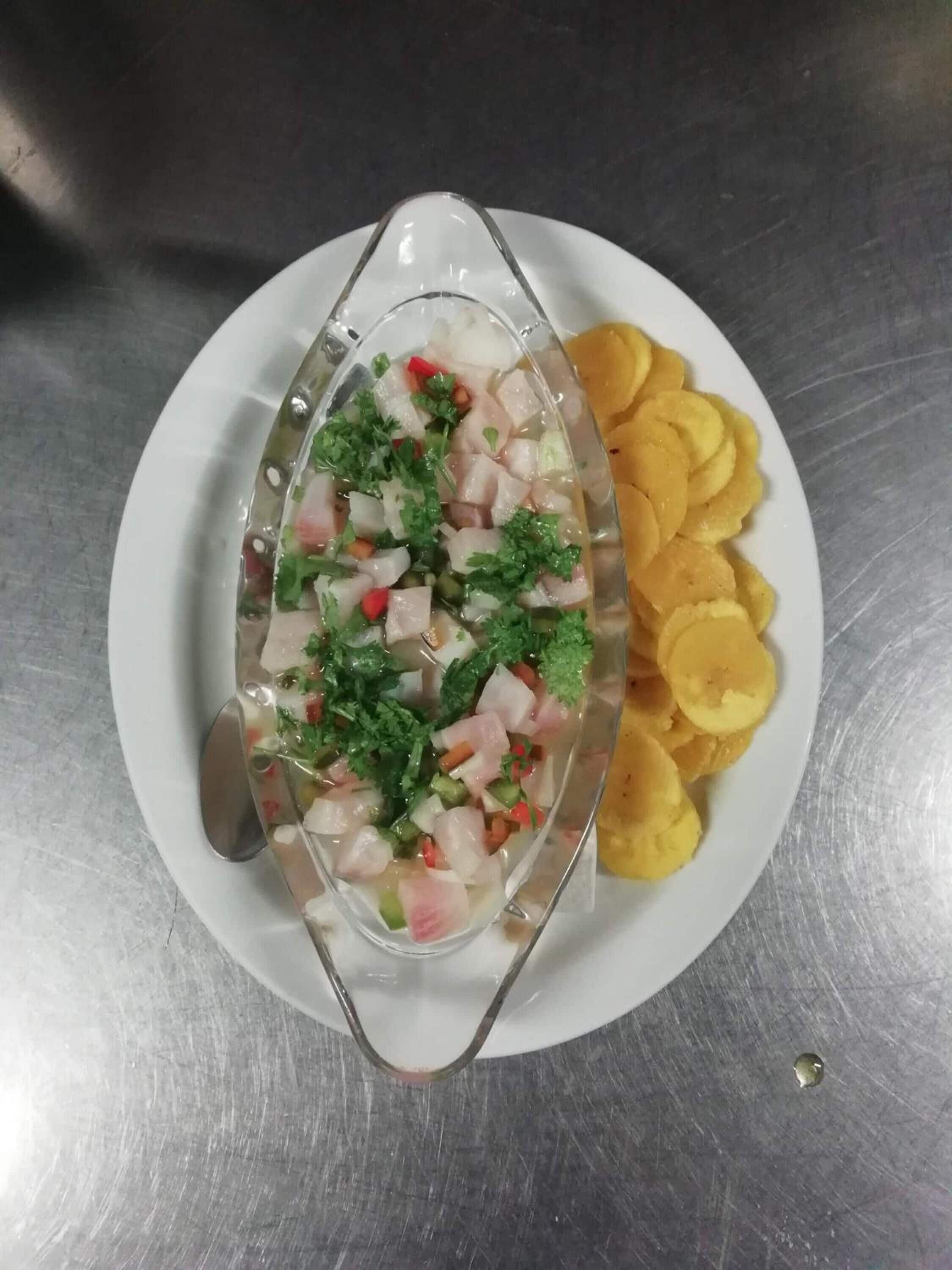 Ein weißer Teller mit einem Meeresfrüchtegericht in einer Glaskugel, dazu gelbe Kartoffelchips.