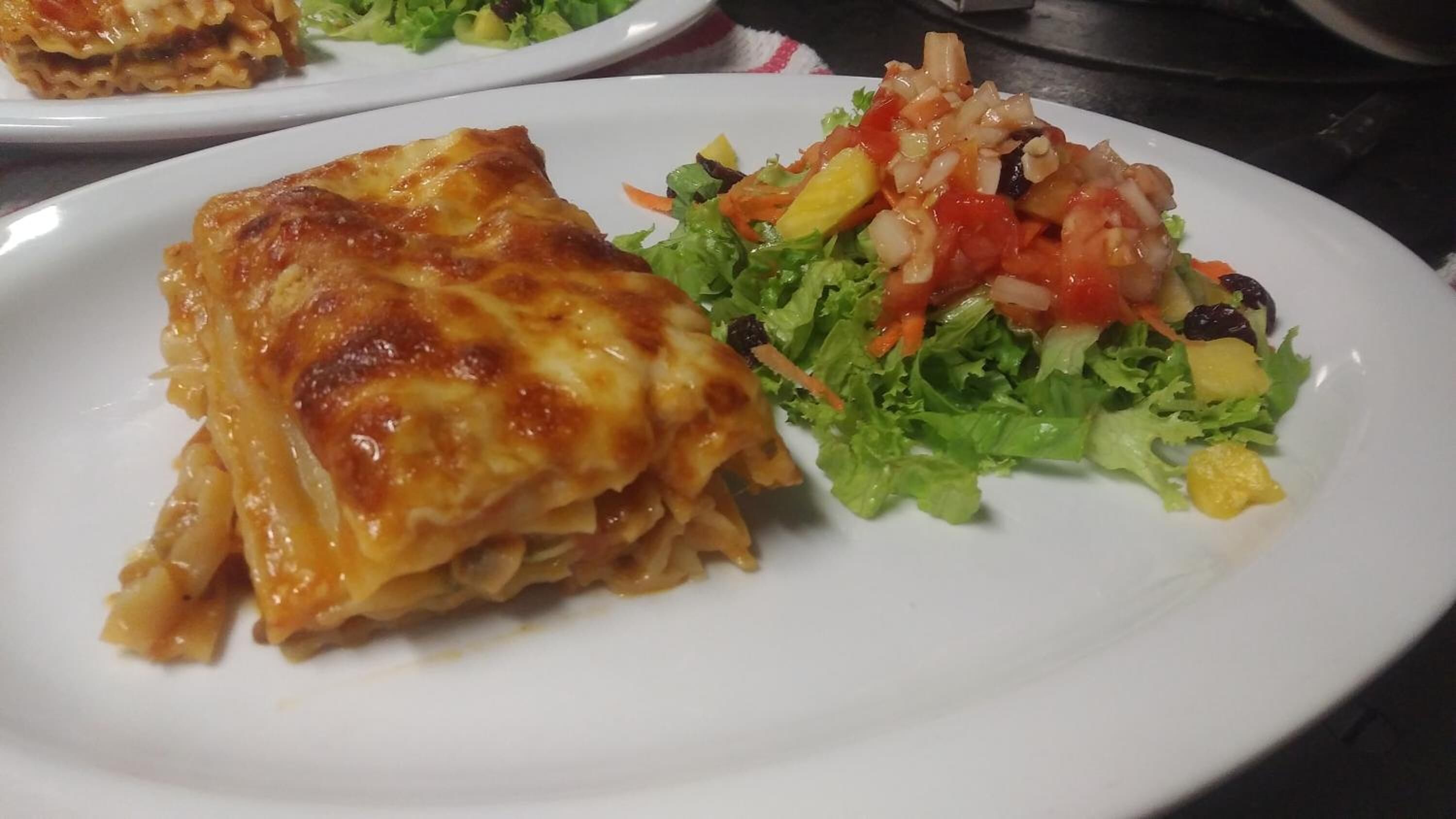 Un plato con una porción de lasaña y una ensalada.