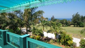 Un balcon offrant une vue sur une pelouse bien entretenue, des palmiers et un ciel bleu dégagé.