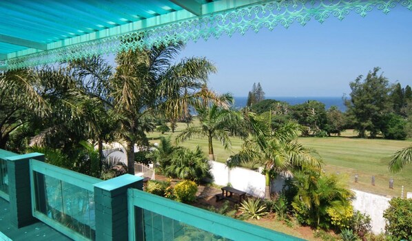 A balcony with a view of a well-maintained lawn, palm trees, and a clear blue sky.