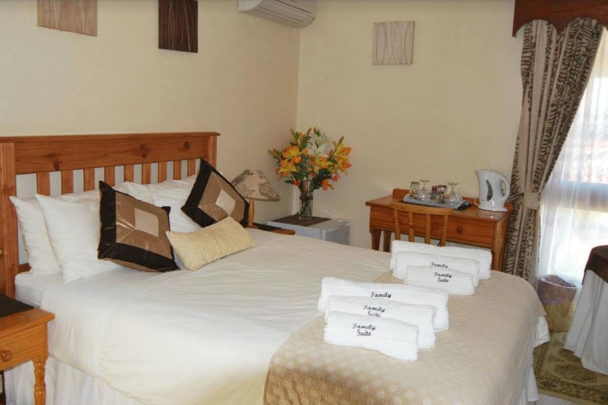 Un lit bien fait, avec une tête de lit en bois, une table de chevet avec une lampe, un vase rempli de fleurs et un plateau avec des serviettes portant l’inscription « Suite familiale » dans une chambre d’hôtel.