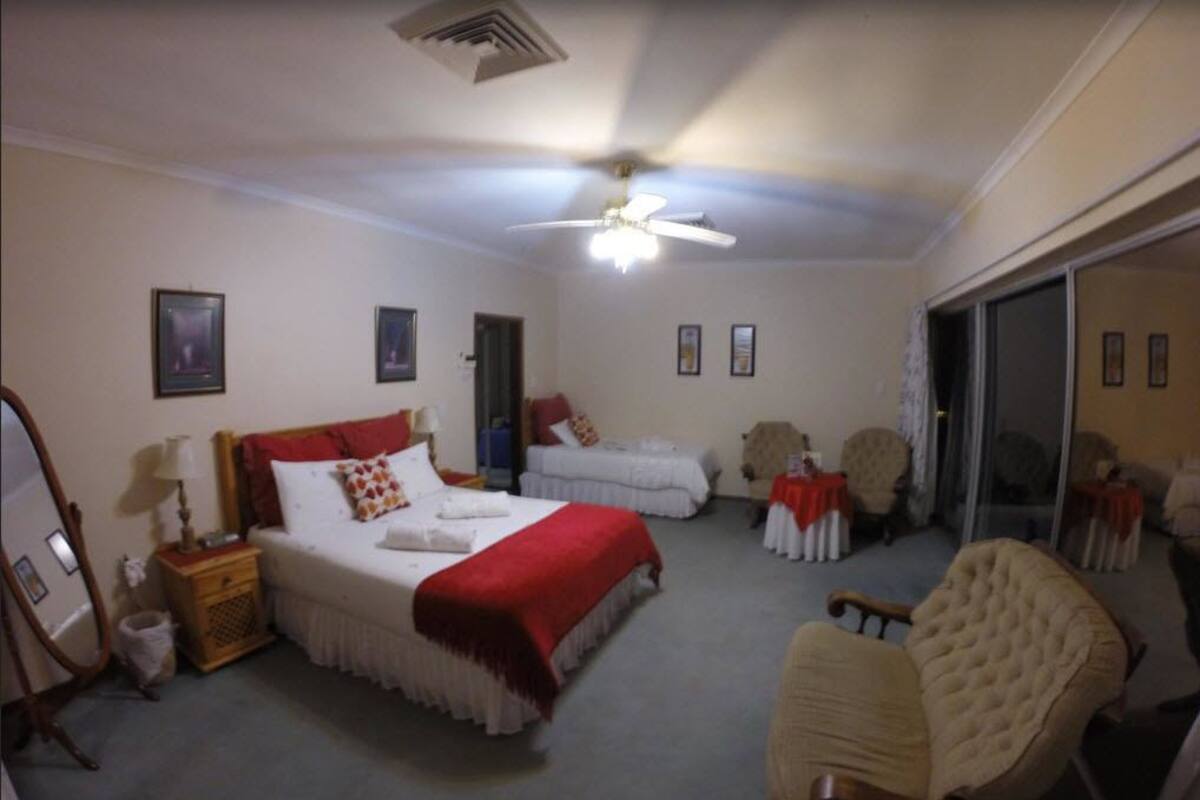 Une chambre d’hôtel avec un grand lit, une chaise, une petite table et un ventilateur de plafond.