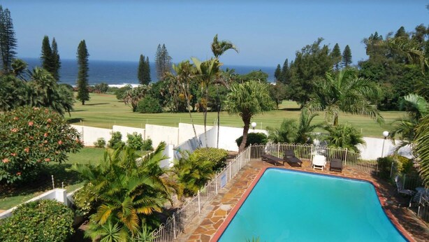 Une piscine avec vue sur l’océan, entourée de palmiers et bordée d’une pelouse bien entretenue.