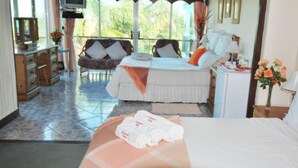 Une chambre d’hôtel comprenant un lit, un petit coin salon avec une chaise et une table, un bureau avec une lampe et une vue sur l’extérieur.
