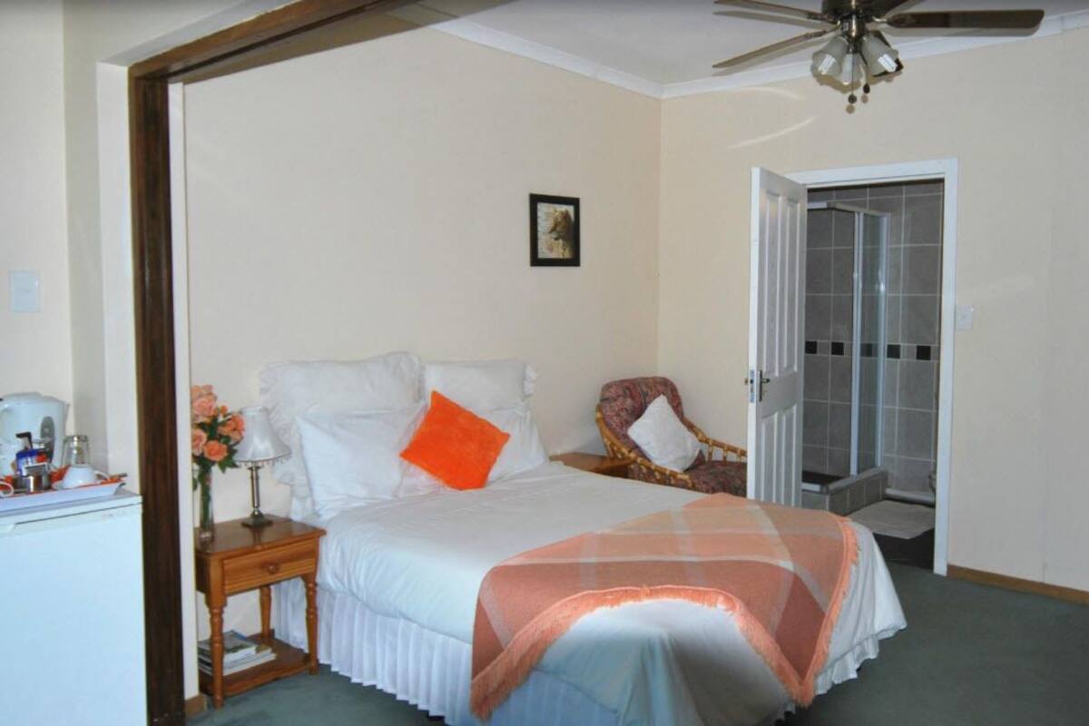 Une chambre à coucher avec un lit, une table de chevet, une chaise, une porte et un ventilateur de plafond.