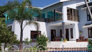 Une maison moderne à deux étages, dotée d’un balcon, d’une piscine et d’une végétation luxuriante.