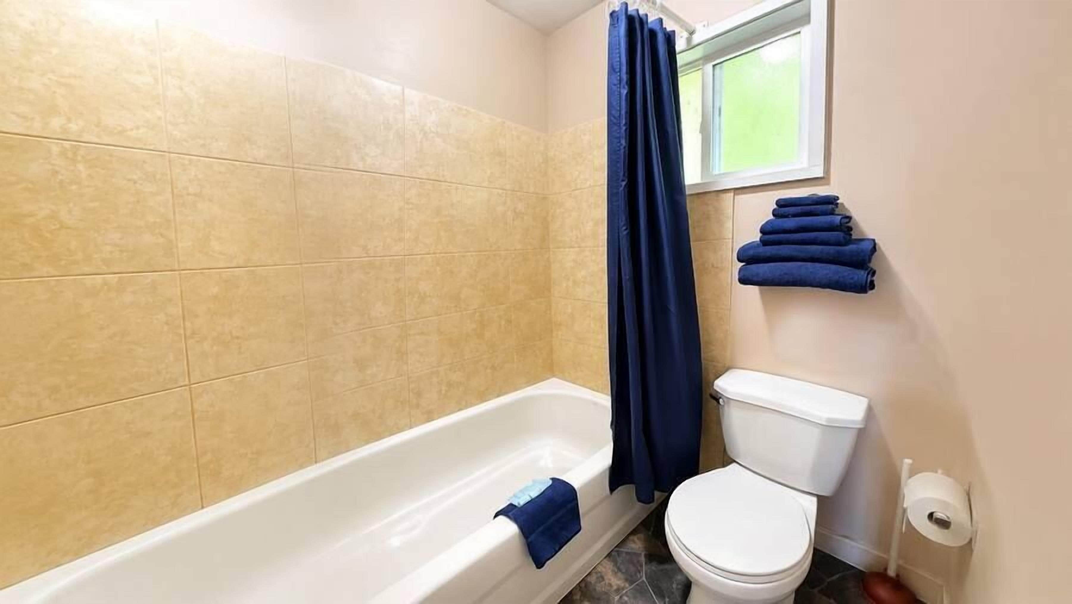 Une salle de bain avec une baignoire, des toilettes et une fenêtre avec des rideaux.