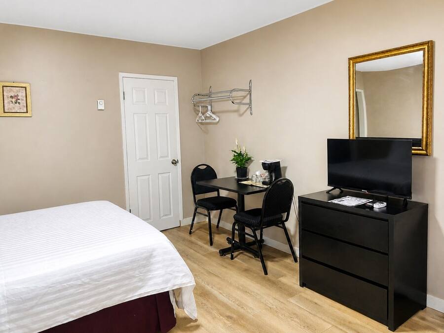 A hotel room with a bed, a desk with a chair, a television, and a mirror.