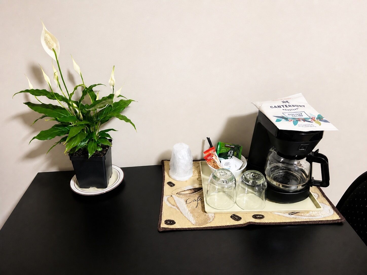 A table with a coffee maker, a potted plant, and a tray with cups and condiments.