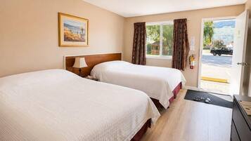 A hotel room with two beds, a wooden headboard, a painting on the wall, and a view of the outside through a door.