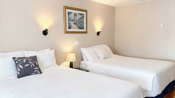 A hotel room with two beds, a painting on the wall, and two wall-mounted lamps.