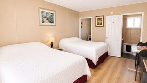 Habitación de hotel con dos camas, un escritorio, una silla, una puerta y un baño pequeño.
