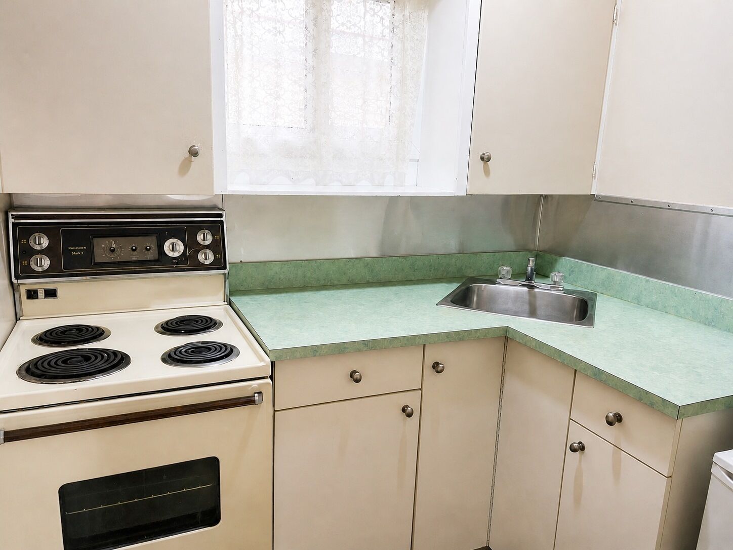 A kitchen with a white stove, green countertop, and stainless steel sink.