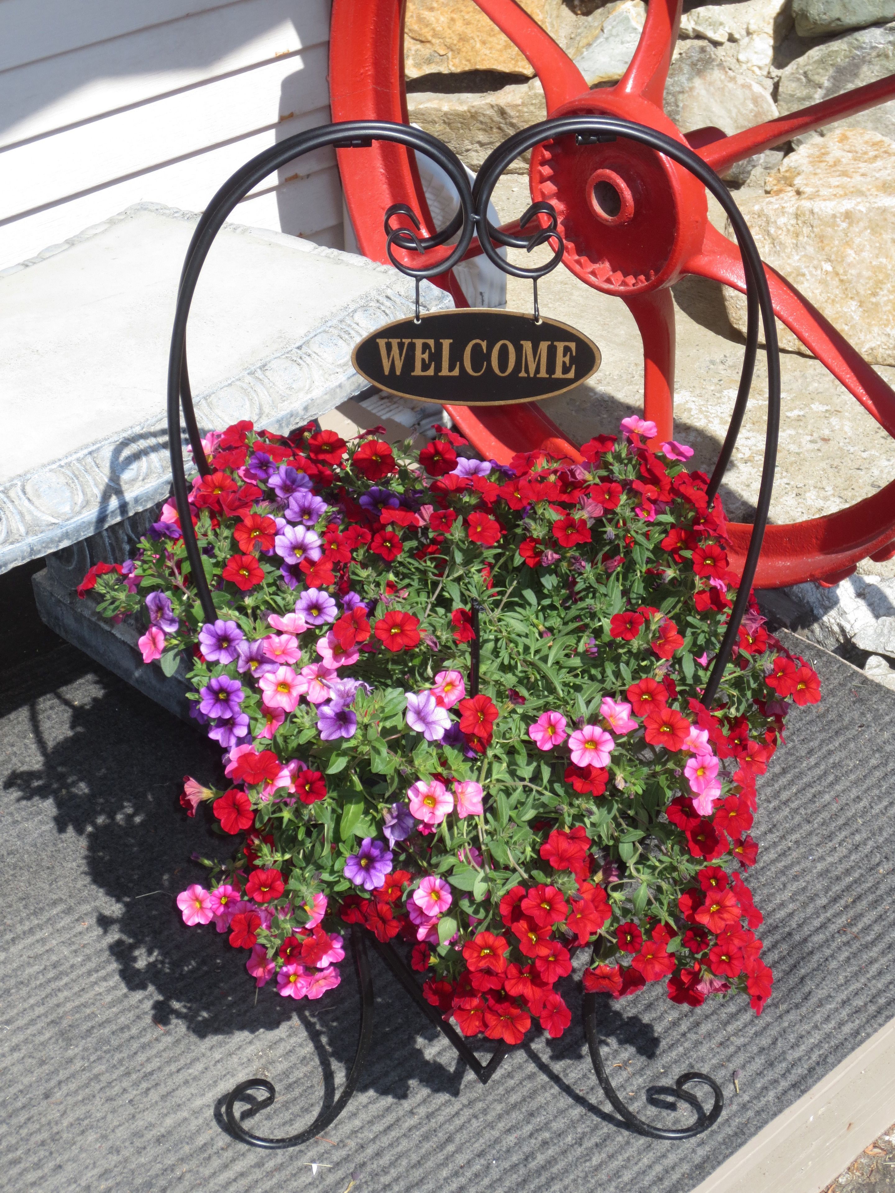 A welcome sign with a flower planter in front of a red metal bench.