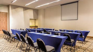 Un salón de conferencias con mesas largas, sillas y una pantalla para proyector.