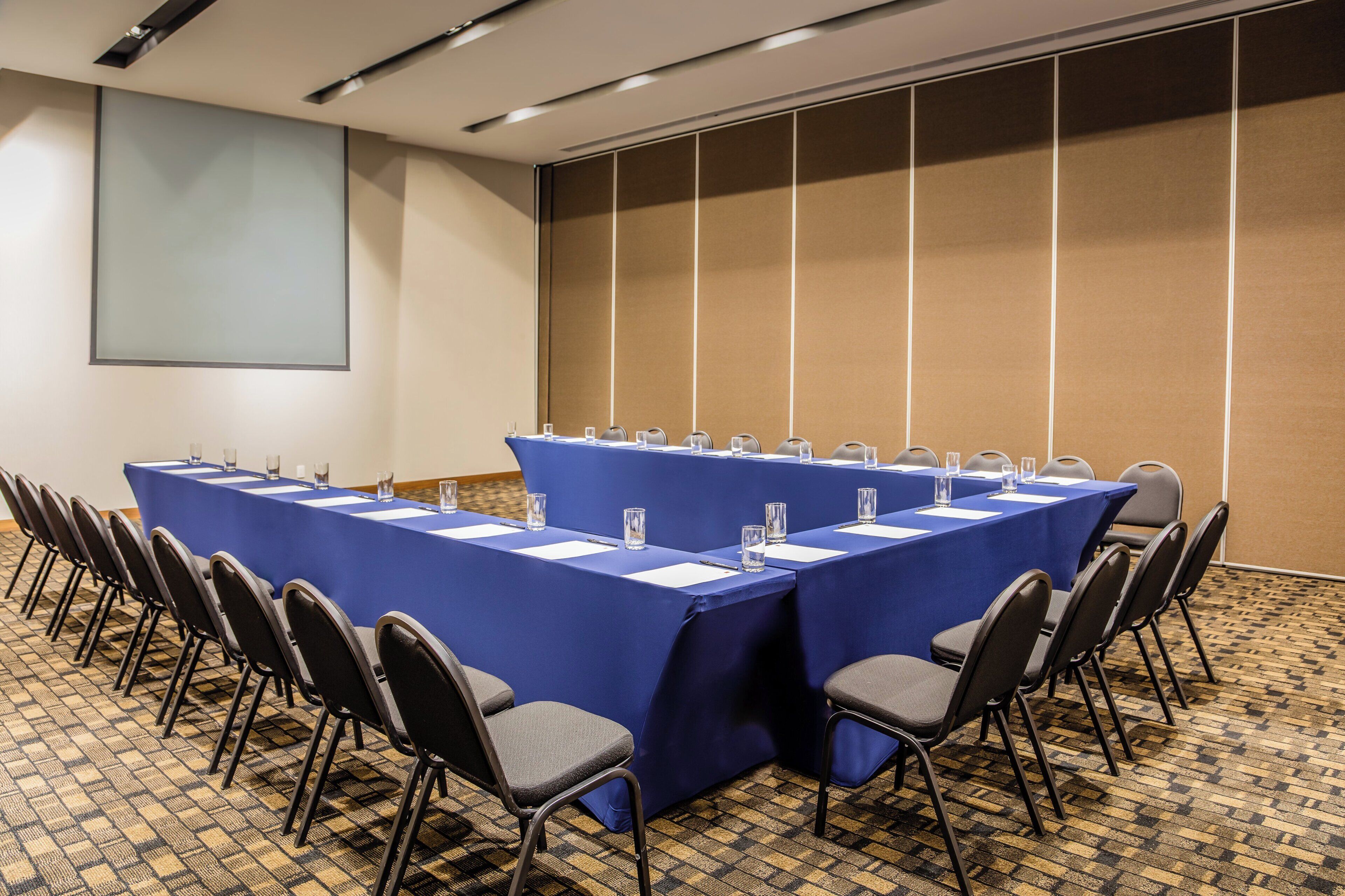 A conference room with a long table, chairs, and a projector screen.