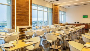 A modern dining area with high ceilings, large windows, and a view of the cityscape.