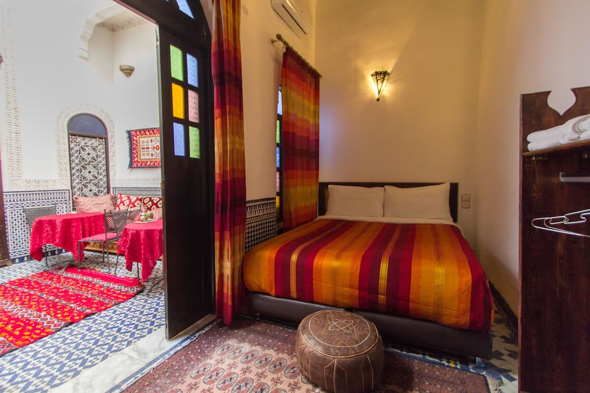Una habitación con cama, una mesa con mantel rojo y un tapete estampado.