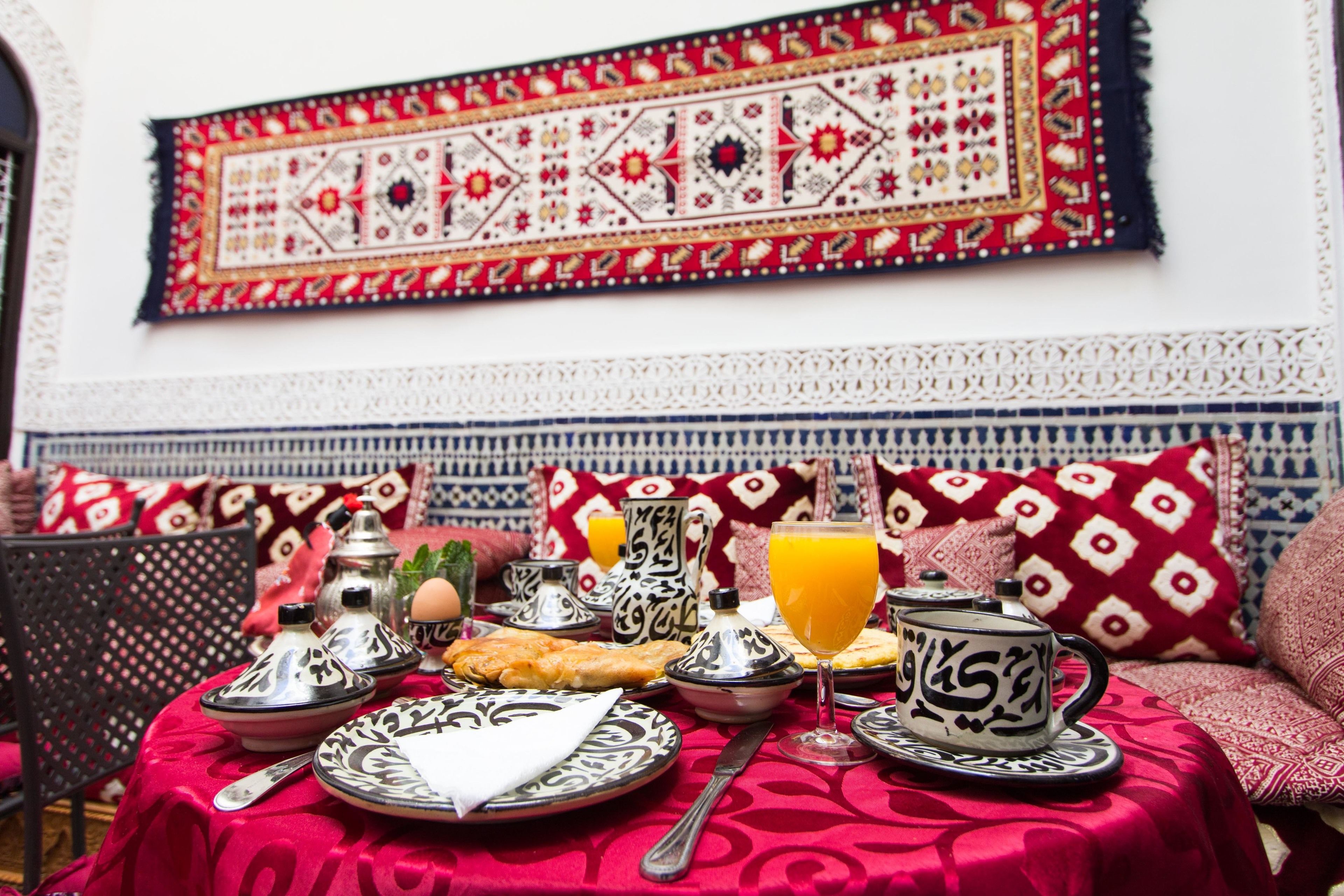 A dining table set with traditional Moroccan tableware, including a teapot, plates, and a glass of orange juice.