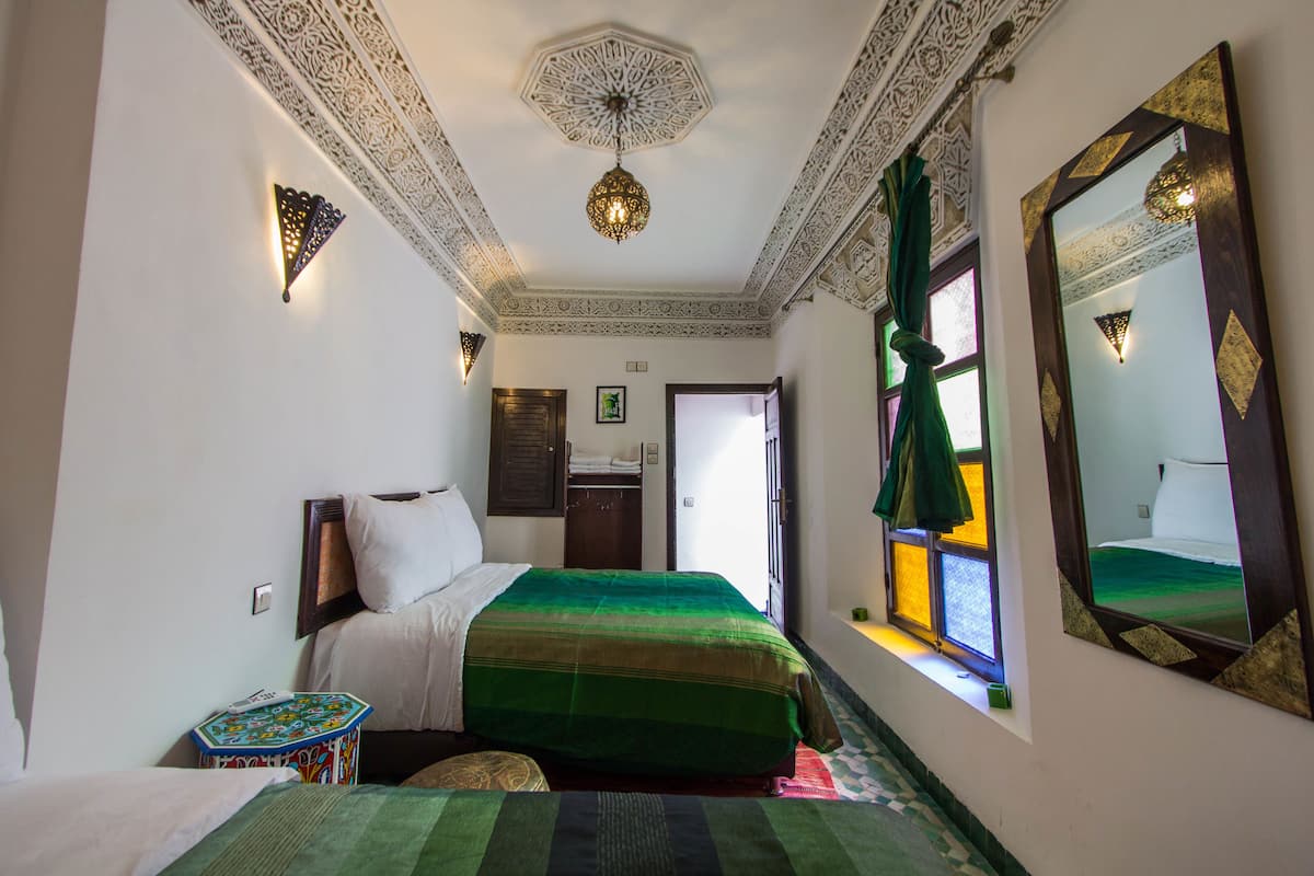 Una habitación con cama, una mesita, un espejo y una ventana con cortinas.