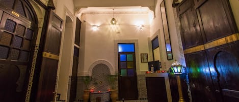 A traditional Moroccan interior with ornate doors, a patterned rug, and a central fountain.
