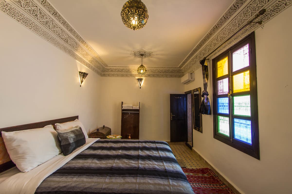 Una habitación con una cama, un techo decorativo, una lámpara de pared y un ventanal con vidrieras.