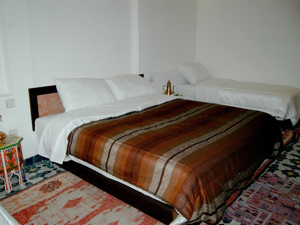 Un lit double avec une couvre-lit à rayures, une petite table de chevet ornée d’un motif floral coloré et un tapis à motifs sur le sol.