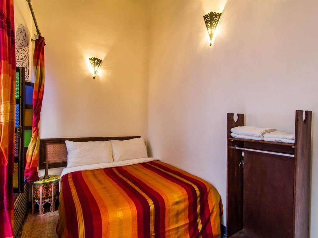 Habitación de hotel con cama, dos lámparas de pared, un armario de madera y una cortina con diseño tradicional.
