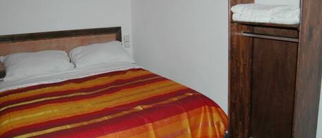 A bed with a striped blanket, a wooden headboard, and a wooden wardrobe with a mirror.