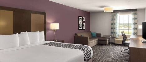 A hotel room with a large bed, a desk, a sofa, and a TV.