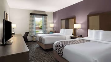 A hotel room with two beds, a desk, a television, and a window with curtains.
