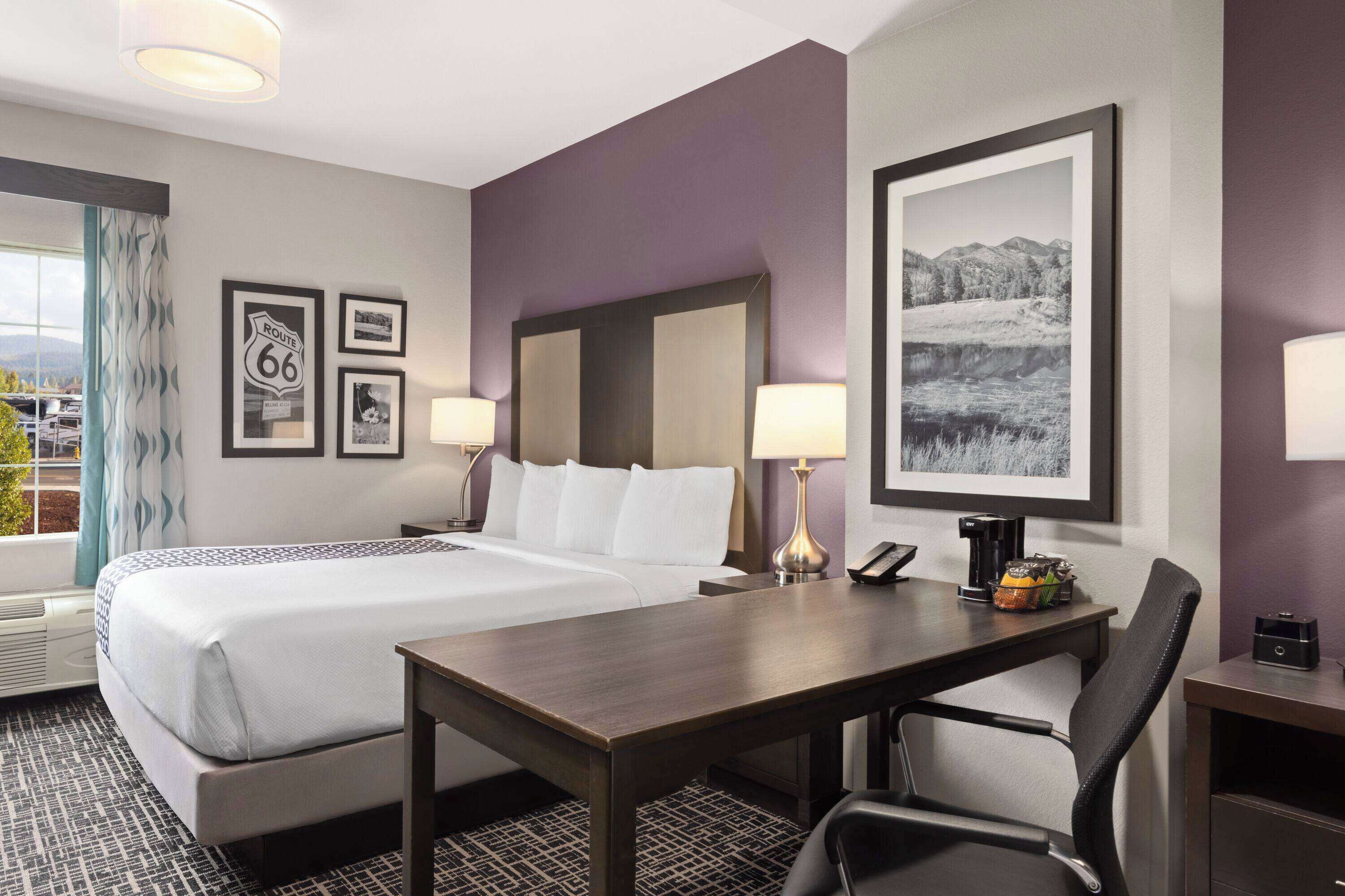 A hotel room with a large bed, two bedside tables with lamps, a desk with a chair, and framed pictures on the walls.
