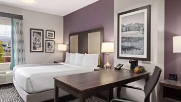 A hotel room with a large bed, two bedside tables with lamps, a desk with a chair, and framed pictures on the walls.