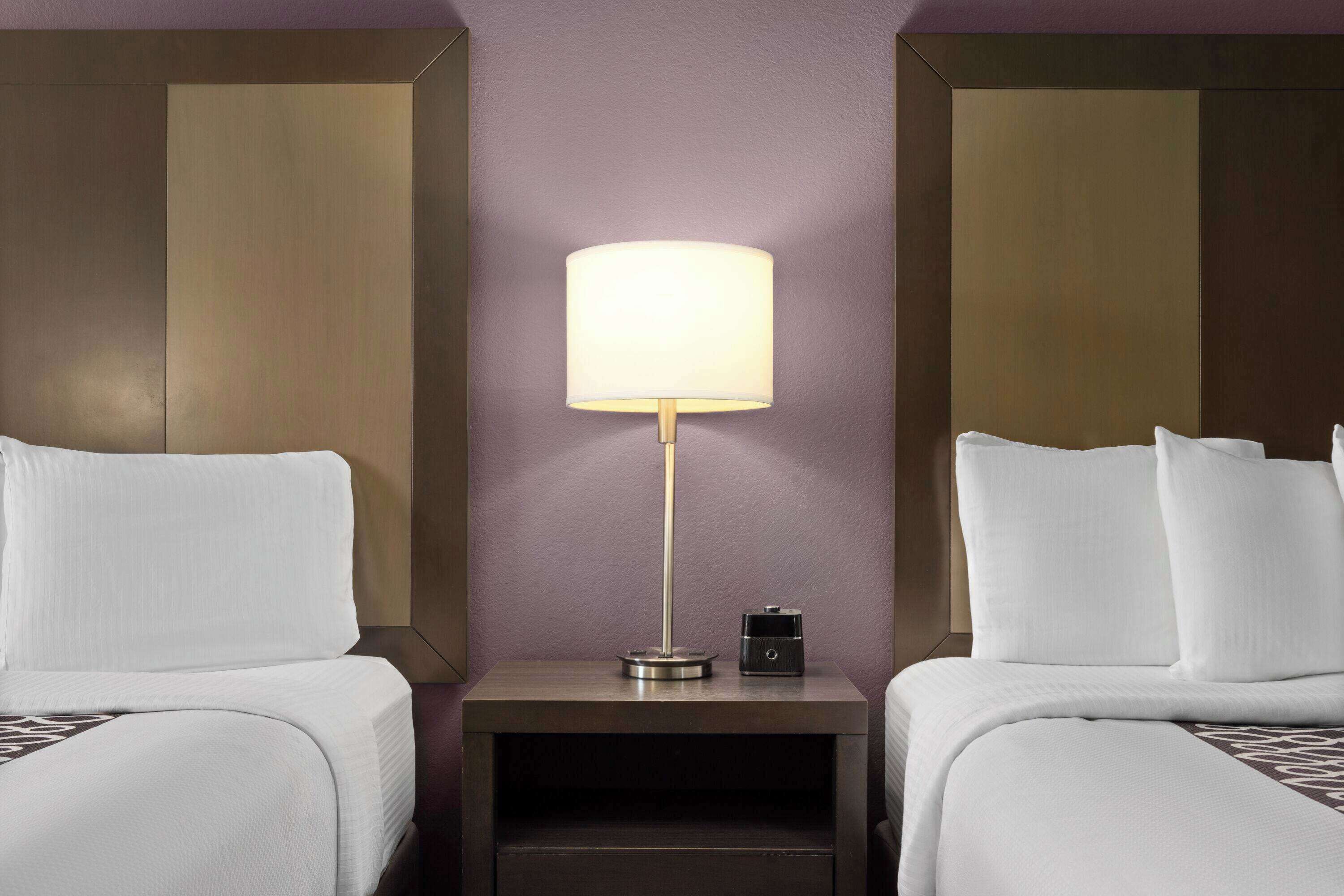 Habitación de hotel con dos camas, una mesita de noche con lámpara y una pequeña mesa.