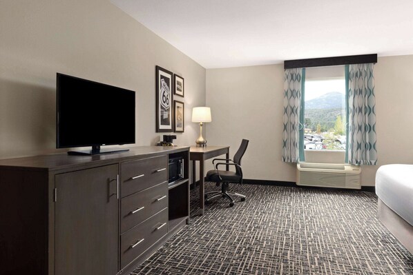 A hotel room with a flat-screen TV, a desk with a chair, a lamp, a bed, and a window with curtains. - La Quinta Inn & Suites by Wyndham Williams-Grand Canyon Area (Williams)