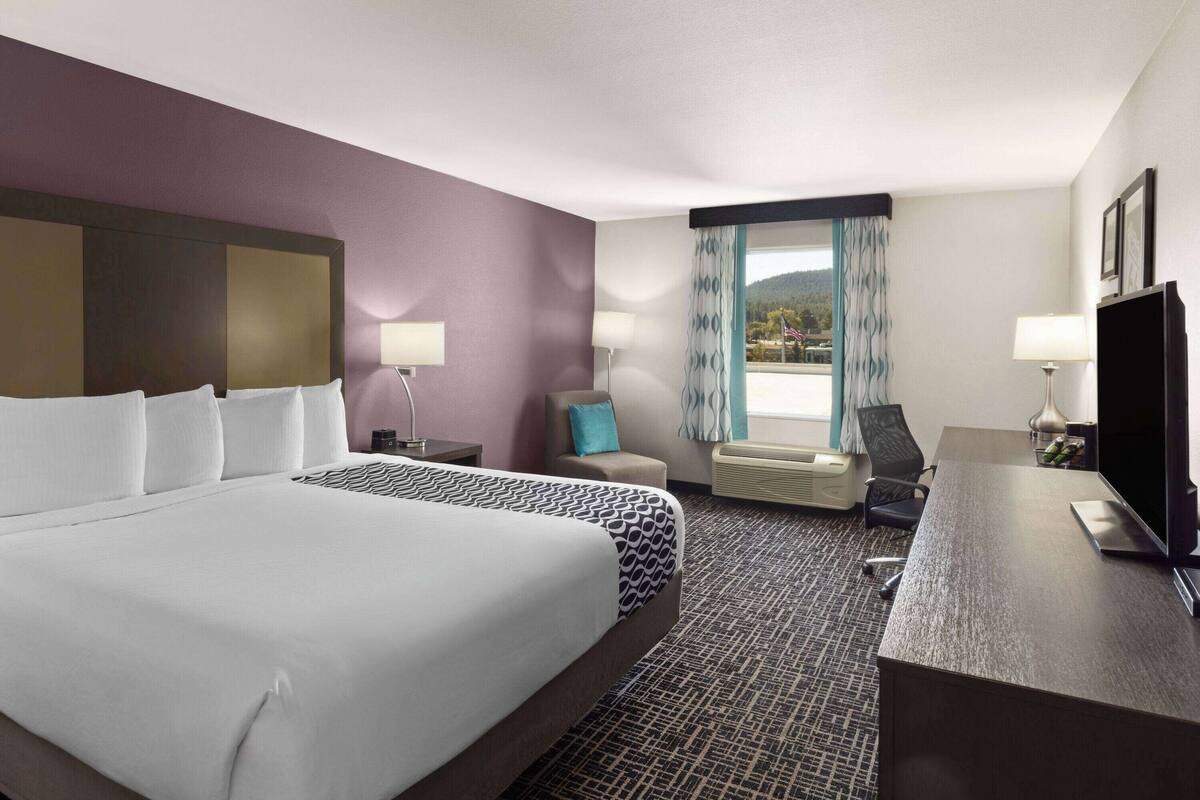 A hotel room with a large bed, a desk, a chair, a TV, and a window with curtains.