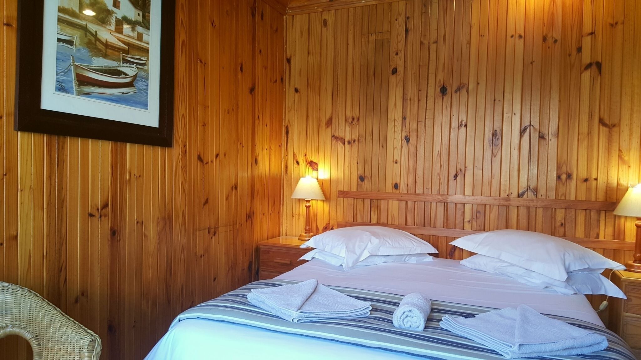A wooden-paneled room with a bed, two bedside lamps, and a framed picture on the wall.