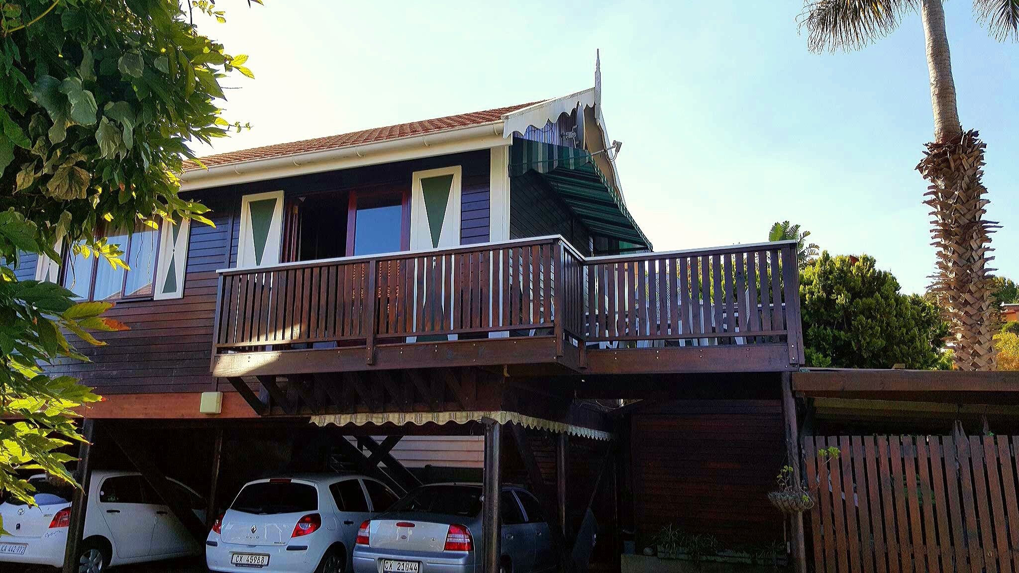 A two-story house with a balcony, a garage with two cars, and a wooden fence.