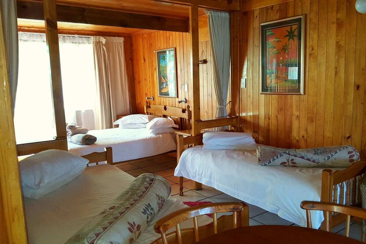 Une cabane en bois avec deux lits, une table à manger et une chaise en osier.