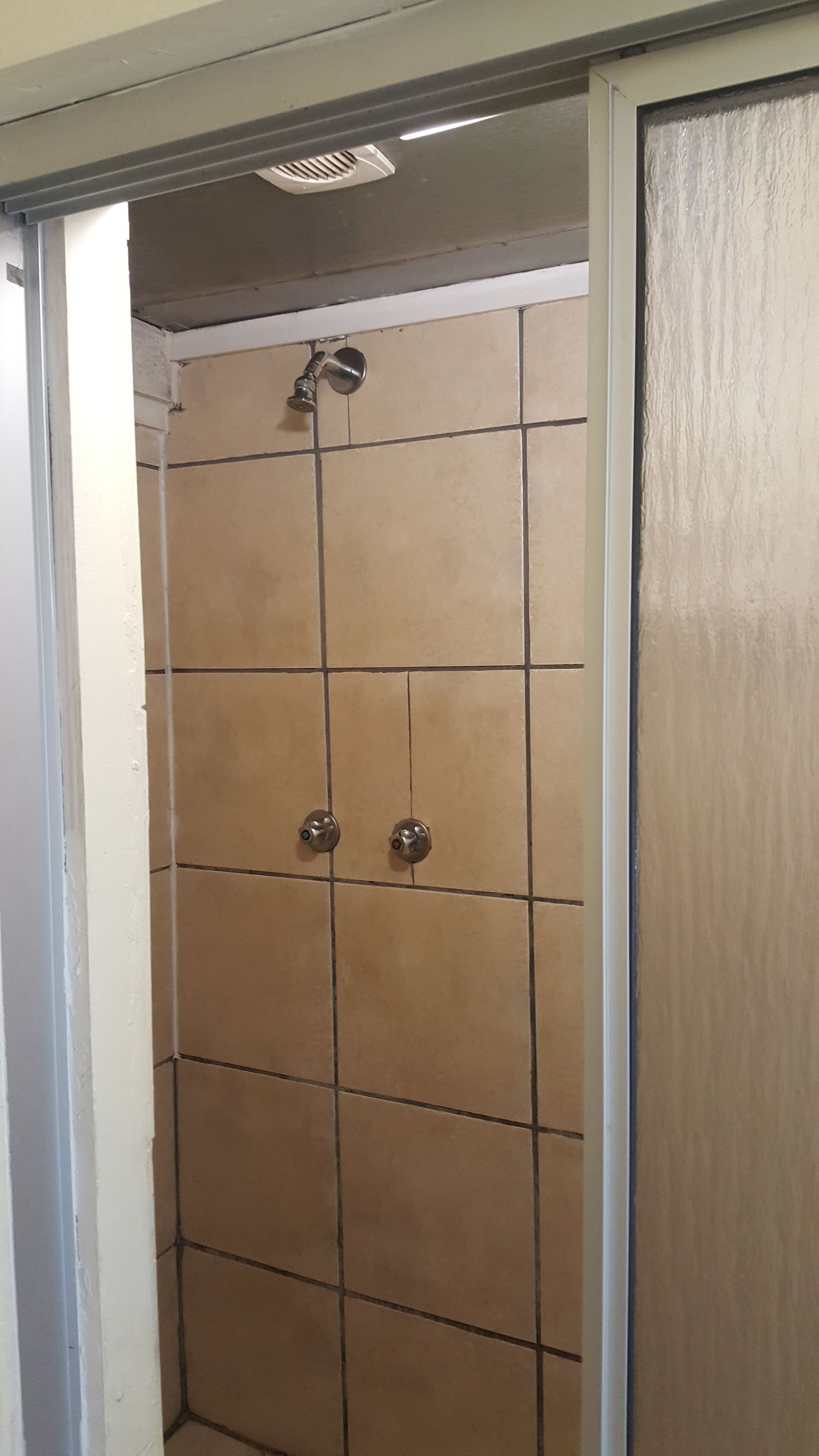 Eine Duschkabine mit gefliesten Wänden, einer Duschbrause und zwei Armaturen.