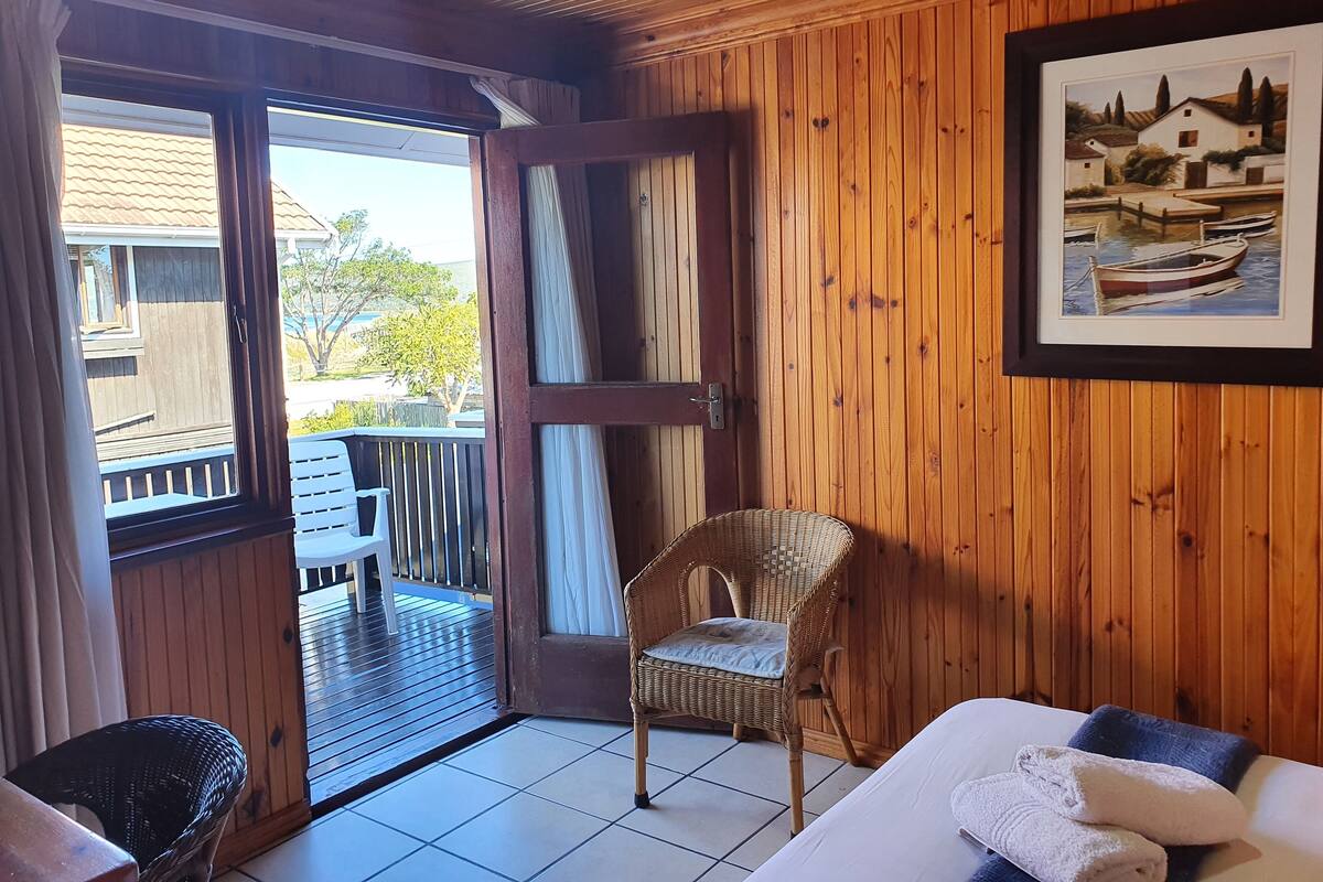Un intérieur en bois avec un balcon, une chaise en osier, un canapé blanc et un tableau encadré.