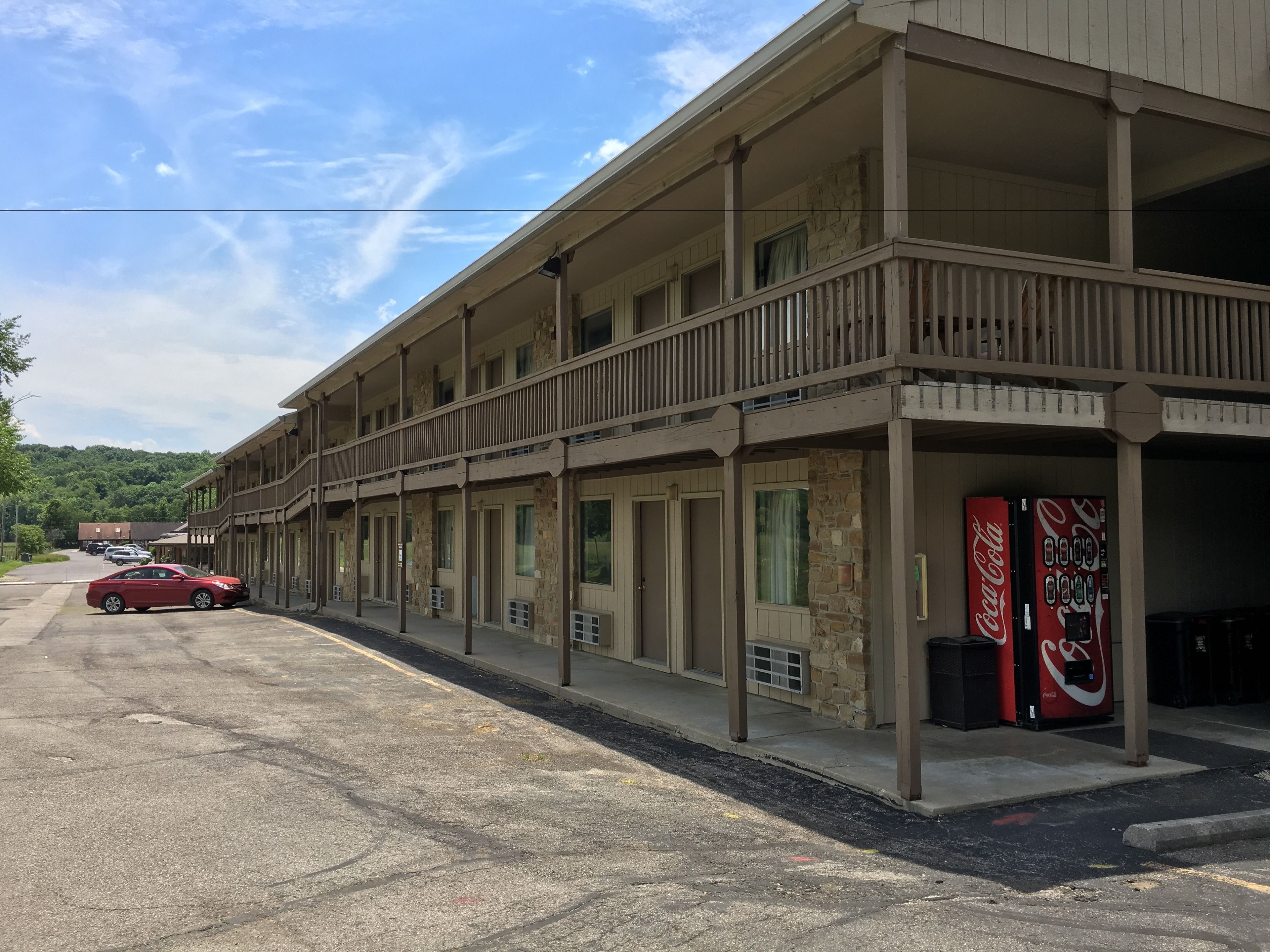 Um motel com várias varandas, uma máquina de refrigerantes Coca-Cola e um estacionamento com um carro vermelho.