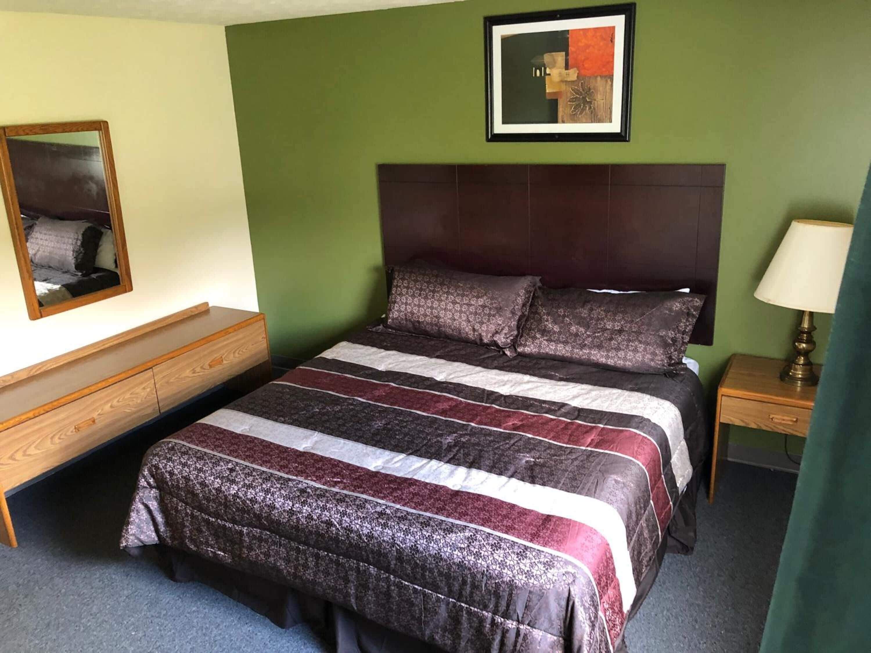 A bedroom with a bed, a nightstand, a dresser, a mirror, and a framed picture on the wall.