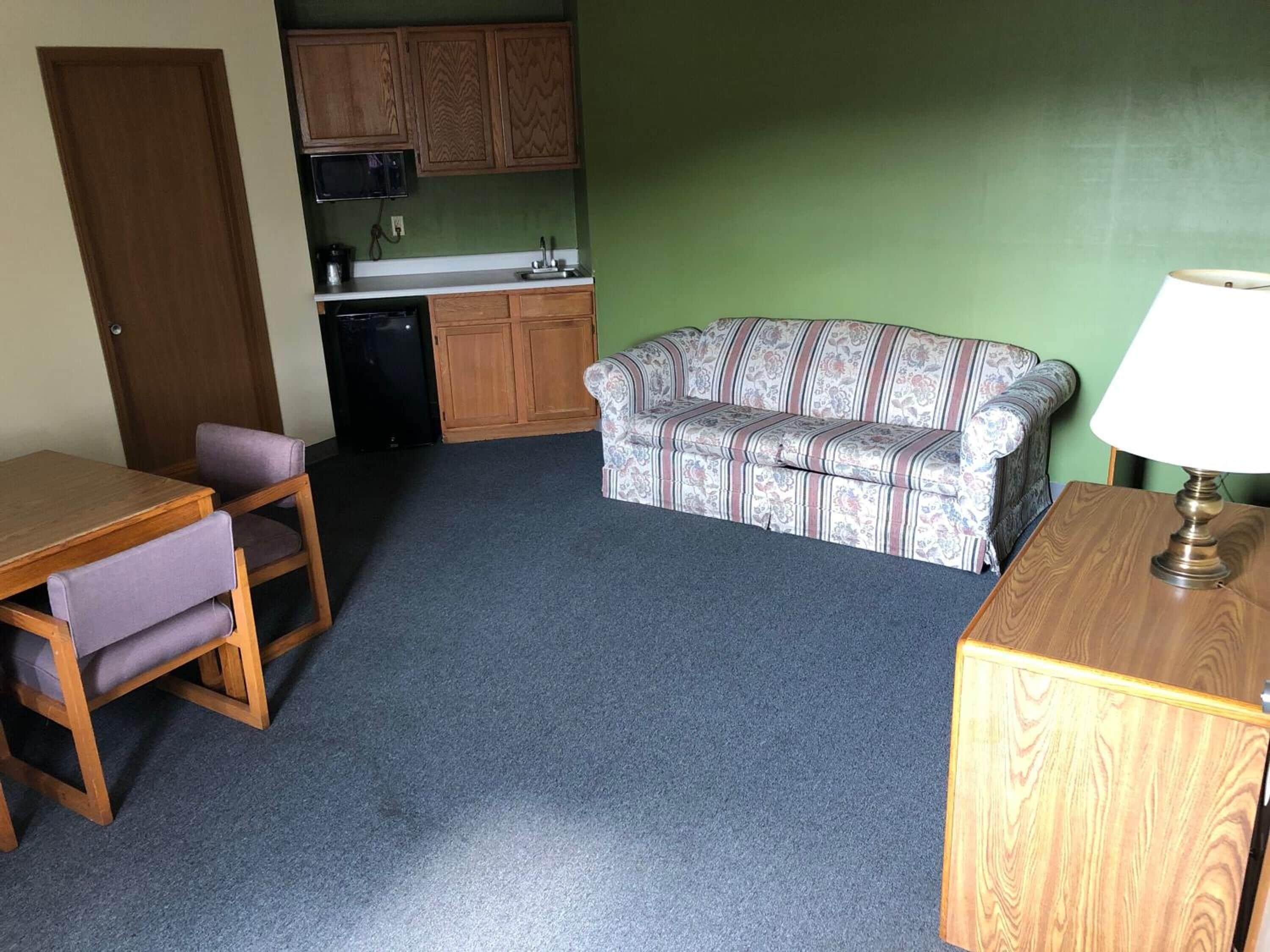 A compact living space with a kitchenette, a sofa, a dining table with chairs, and a lamp.
