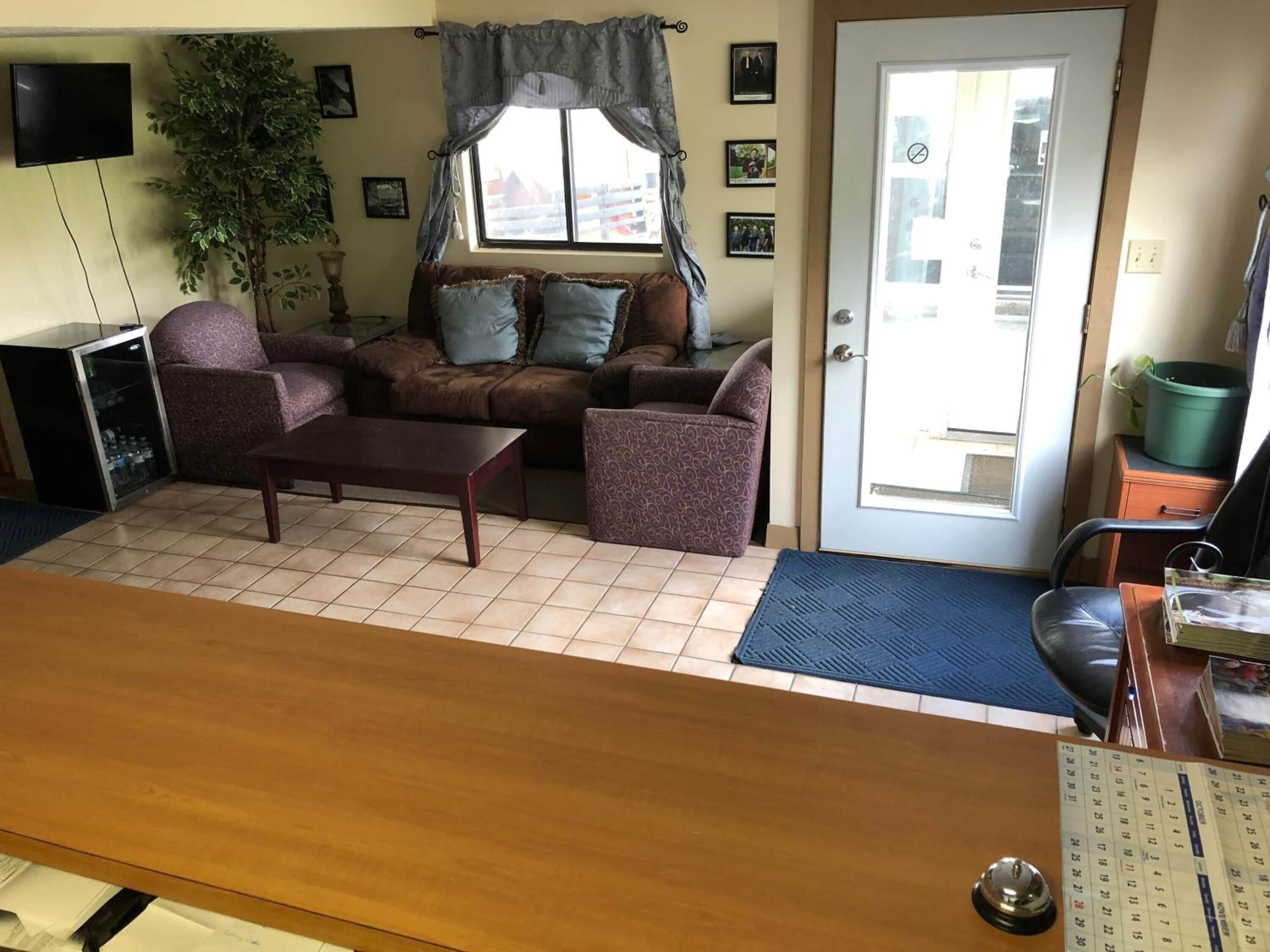 A living room with a brown sofa, patterned armchairs, a coffee table, a television, and a refrigerator.