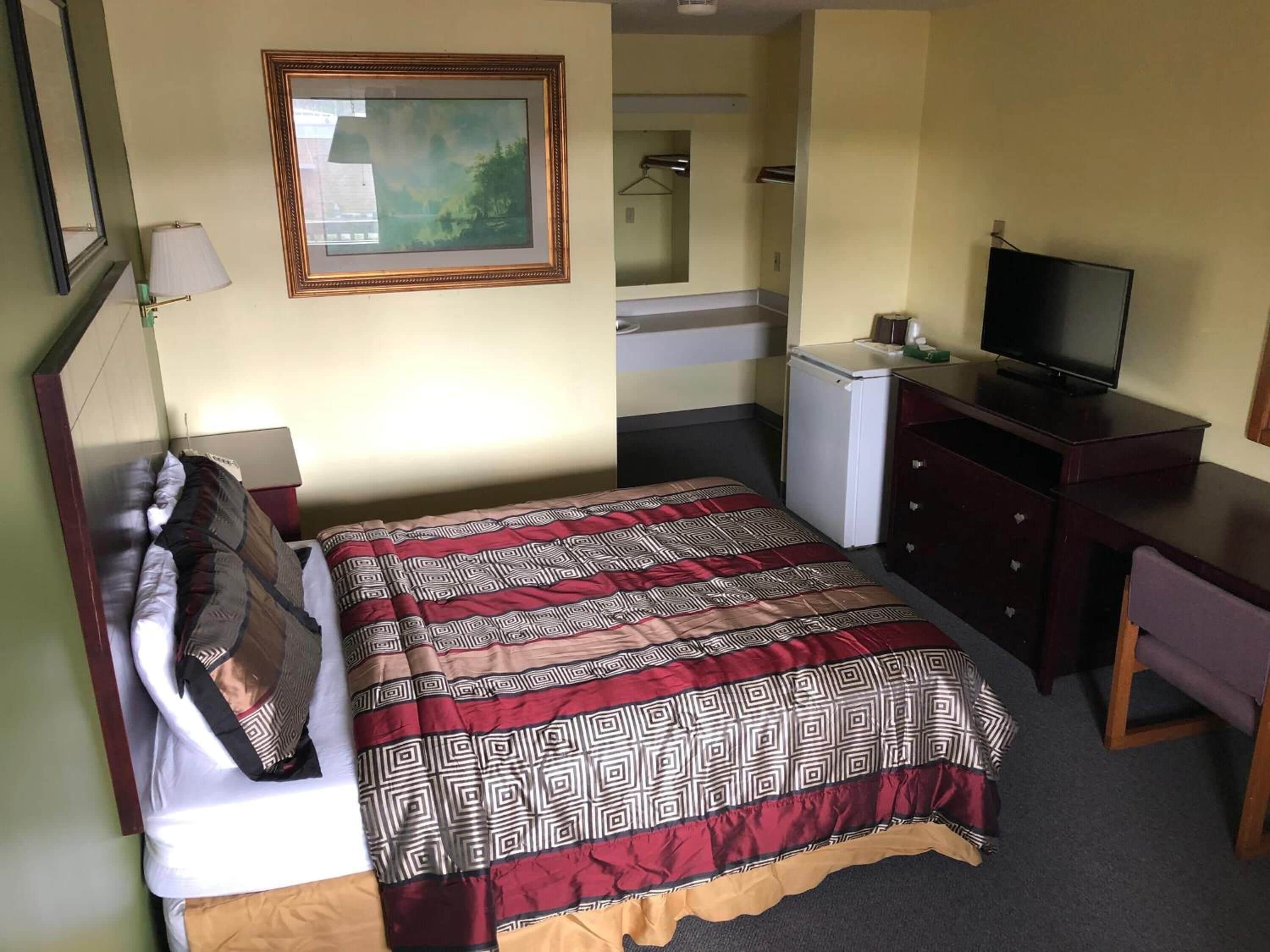 Een hotelkamer met een bed, een bureau, een televisie, een spiegel en een kleine koelkast.