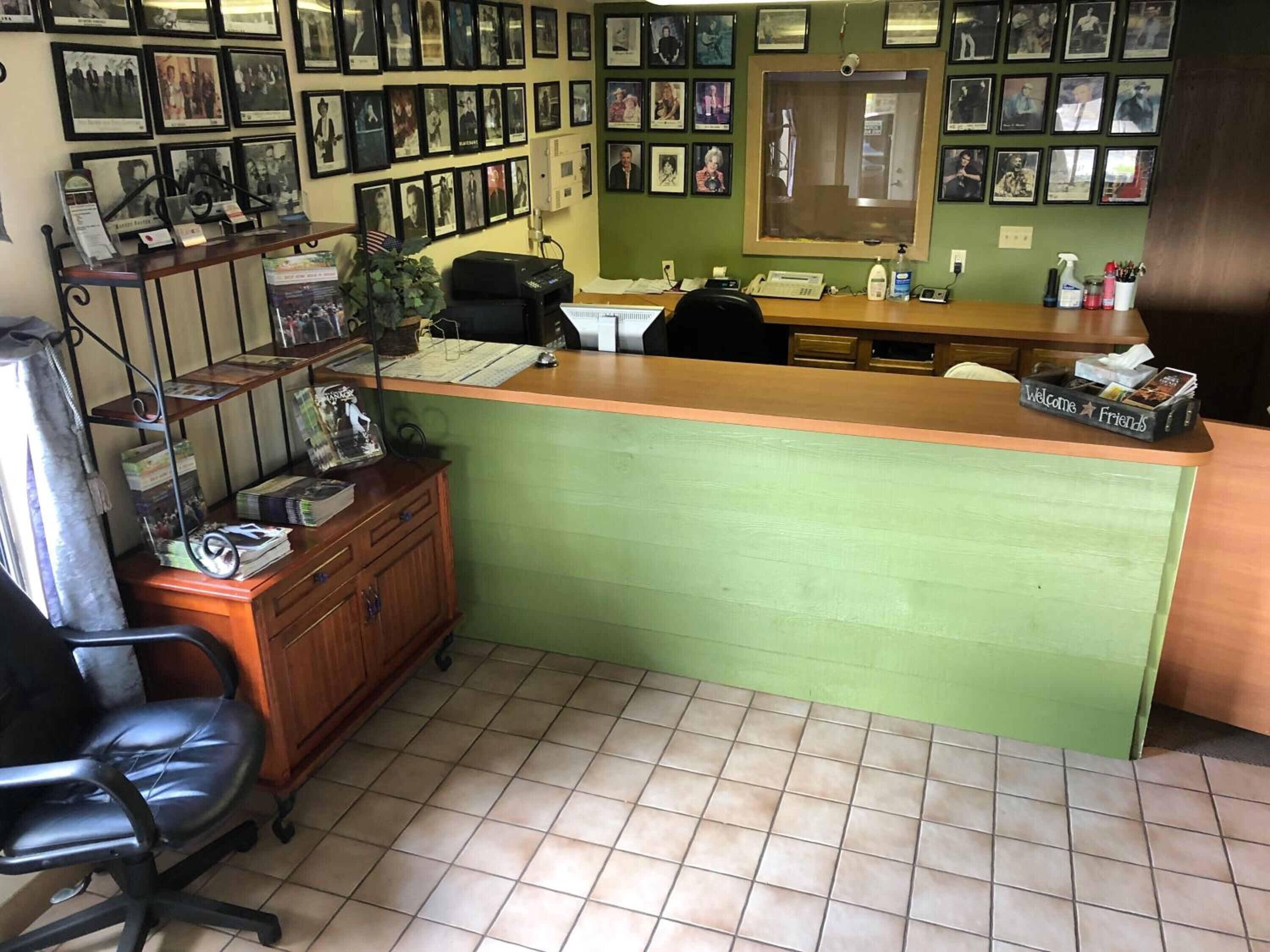 A reception area with a green counter, a desk, a chair, a telephone, and a wall adorned with framed photographs.